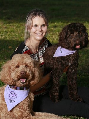 Jess sitting on the grass with two dogs each wearing a scarf
